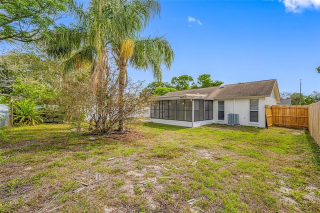 rear view of property with a yard, central air condition unit, stucco siding, a sunroom, and a fenced backyard