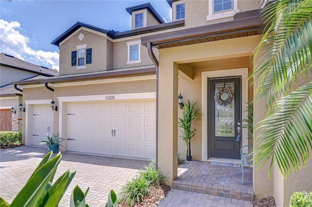 doorway to property with stucco siding, a garage, and decorative driveway