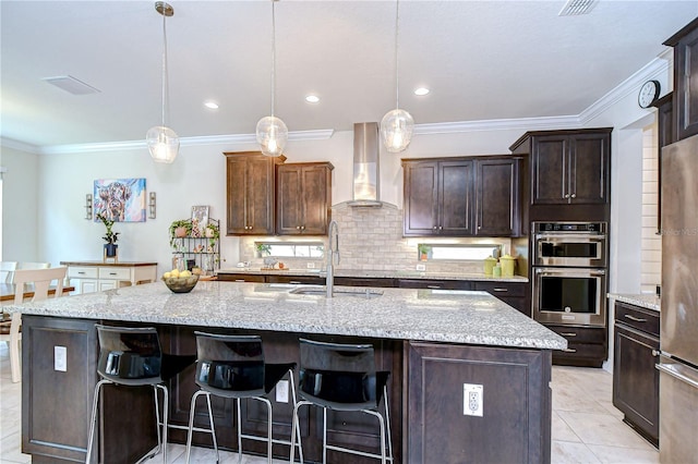 kitchen with wall chimney range hood, a sink, ornamental molding, tasteful backsplash, and a kitchen bar