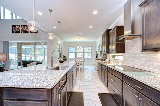 kitchen featuring a sink, wall chimney range hood, a center island with sink, backsplash, and crown molding
