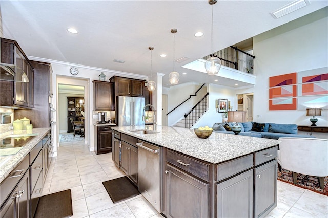 kitchen with a sink, stainless steel appliances, dark brown cabinetry, a center island with sink, and pendant lighting