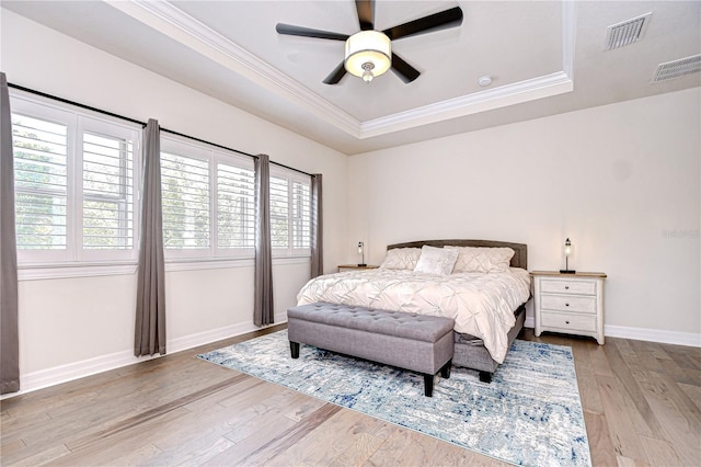 bedroom featuring a raised ceiling, multiple windows, ornamental molding, wood finished floors, and baseboards