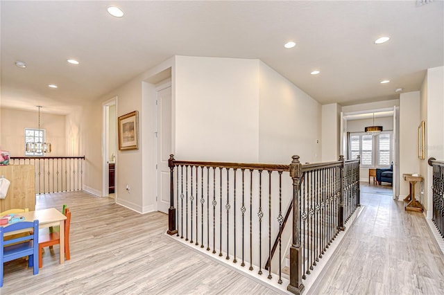 corridor with an upstairs landing, a chandelier, baseboards, light wood-style floors, and recessed lighting