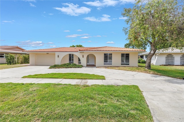mediterranean / spanish-style home with curved driveway, stucco siding, a tile roof, a front yard, and a garage