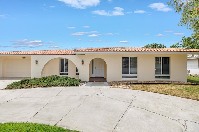mediterranean / spanish-style house with a tiled roof, stucco siding, an attached garage, and concrete driveway