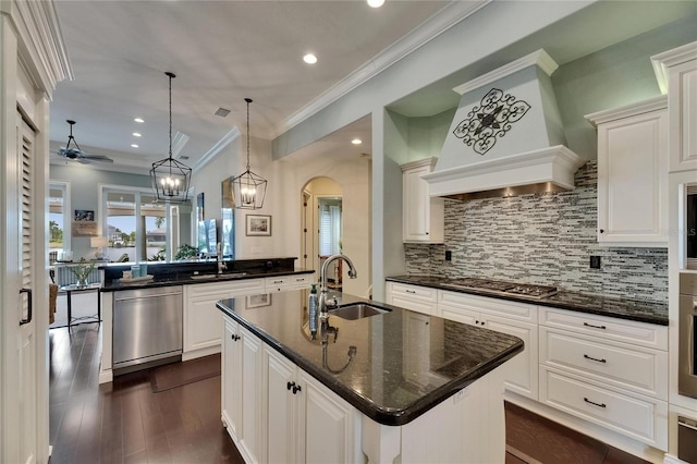 kitchen with a sink, appliances with stainless steel finishes, custom range hood, a center island with sink, and backsplash