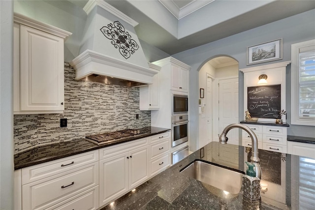 kitchen featuring stainless steel appliances, a sink, custom range hood, ornamental molding, and decorative backsplash