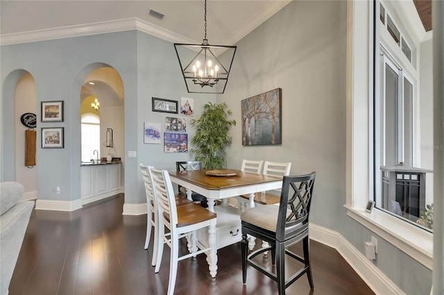dining space featuring dark wood finished floors, arched walkways, a chandelier, baseboards, and ornamental molding