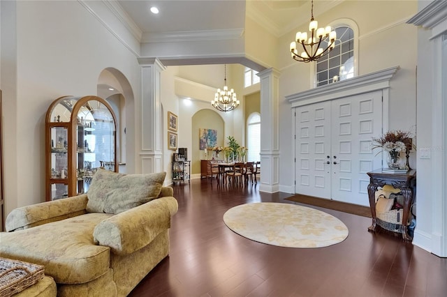 entrance foyer featuring a chandelier, ornamental molding, arched walkways, a high ceiling, and ornate columns