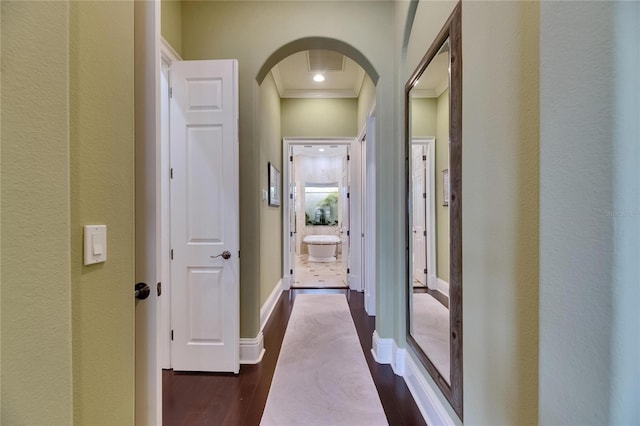 corridor with arched walkways, crown molding, dark wood-style floors, and baseboards