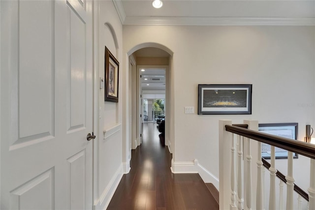corridor featuring arched walkways, an upstairs landing, ornamental molding, dark wood-type flooring, and baseboards