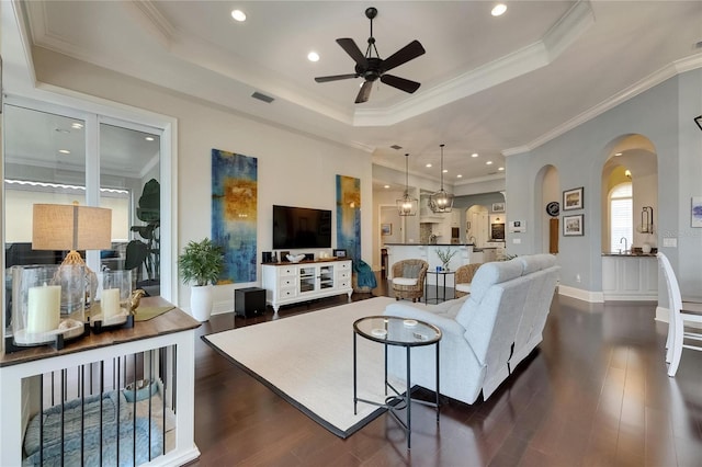 living area with a tray ceiling, arched walkways, ceiling fan, dark wood-style flooring, and recessed lighting