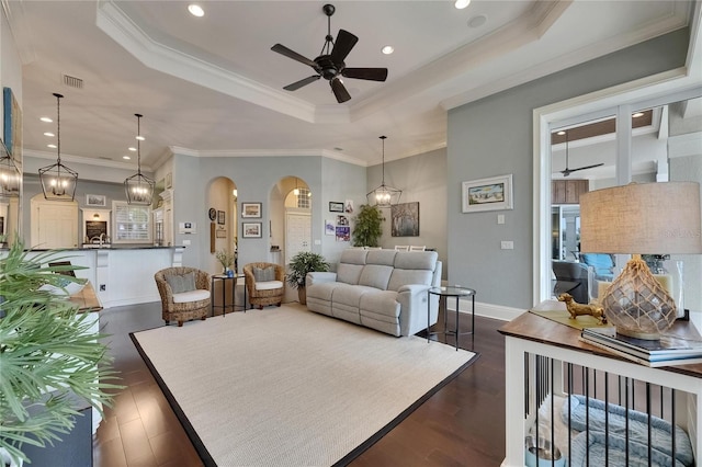 living room with arched walkways, a raised ceiling, dark wood-type flooring, a ceiling fan, and baseboards