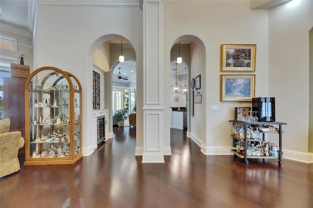 hallway with arched walkways, wood finished floors, ornamental molding, and baseboards
