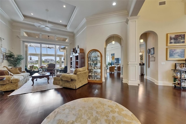 living room with decorative columns, arched walkways, ceiling fan, dark wood-style floors, and a towering ceiling
