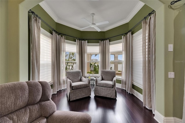 living area featuring arched walkways, ceiling fan, baseboards, crown molding, and dark wood-type flooring