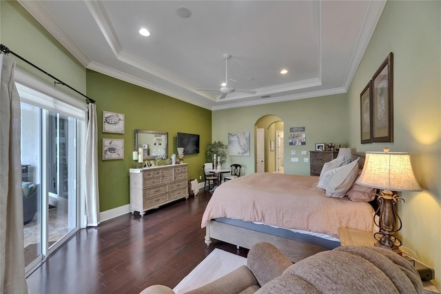 bedroom with a tray ceiling, arched walkways, dark wood-type flooring, ornamental molding, and baseboards