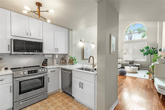 kitchen with appliances with stainless steel finishes, a sink, light countertops, a chandelier, and white cabinetry