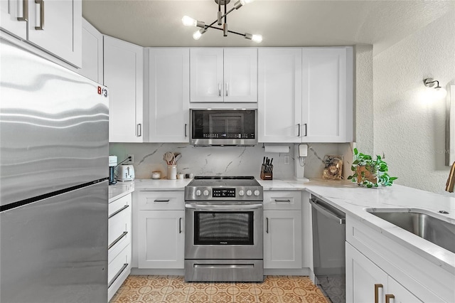kitchen featuring stainless steel appliances, white cabinets, a sink, light stone counters, and a textured wall