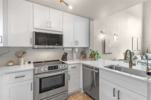 kitchen with appliances with stainless steel finishes, a textured wall, white cabinets, a sink, and light stone countertops