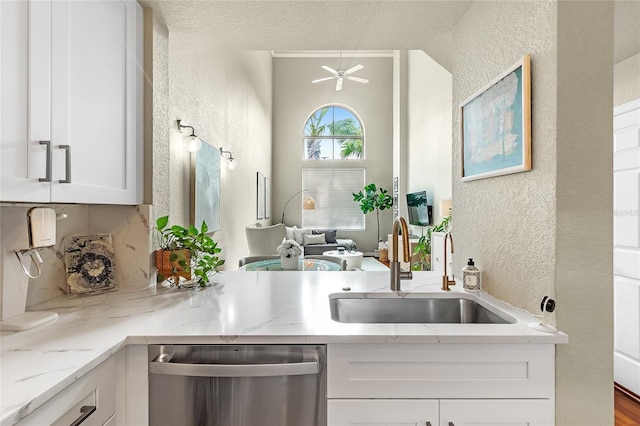kitchen featuring dishwasher, a textured wall, a sink, white cabinetry, and light stone countertops