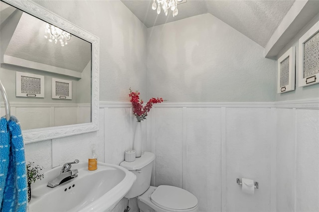 bathroom with a sink, vaulted ceiling, toilet, a chandelier, and wainscoting