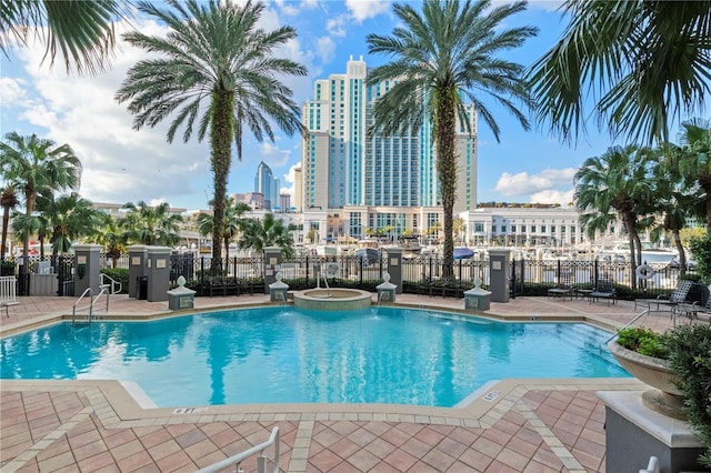 view of pool with fence, a pool with connected hot tub, a patio area, and a skyline view