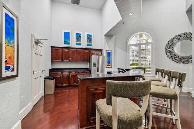 bar featuring stainless steel refrigerator with ice dispenser, a high ceiling, dark wood-type flooring, and baseboards