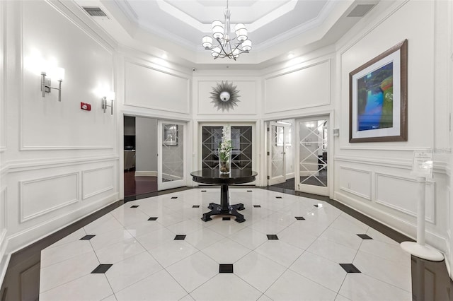 tiled foyer entrance featuring a decorative wall, a chandelier, inlaid floor details, ornamental molding, and a raised ceiling