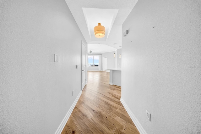 hall with light wood-type flooring, baseboards, and a textured wall