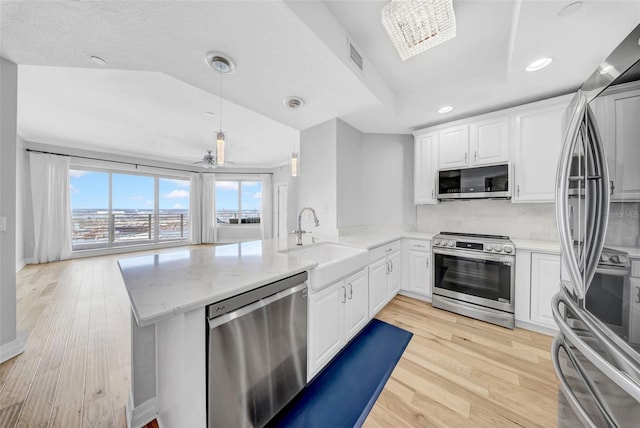 kitchen with a peninsula, stainless steel appliances, light wood-style flooring, and a sink