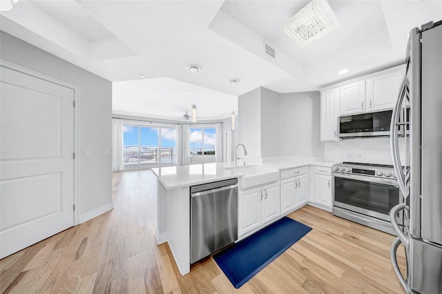 kitchen with a peninsula, a sink, visible vents, a raised ceiling, and appliances with stainless steel finishes