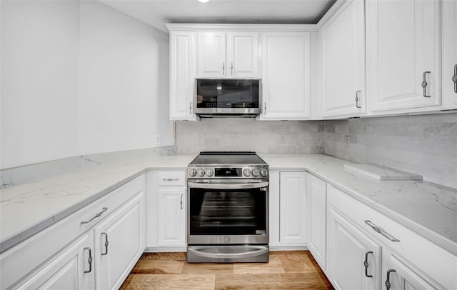 kitchen featuring light stone countertops, white cabinetry, decorative backsplash, stainless steel appliances, and light wood-type flooring