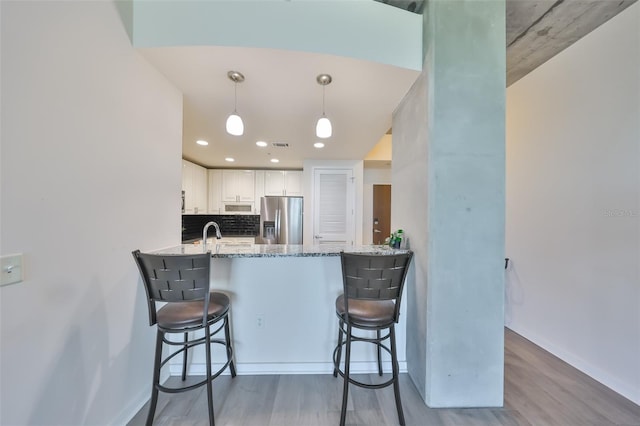 kitchen with stainless steel fridge with ice dispenser, baseboards, wood finished floors, and white cabinets