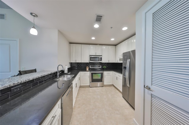 kitchen featuring a sink, dark stone counters, stainless steel appliances, white cabinets, and backsplash