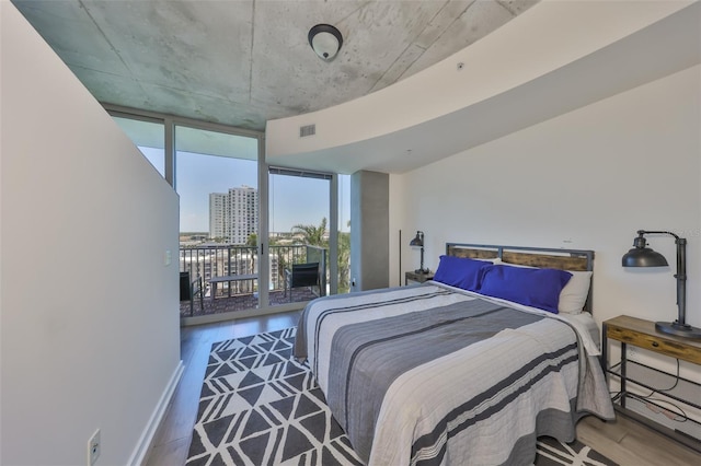 bedroom featuring access to outside, a wall of windows, visible vents, and wood finished floors