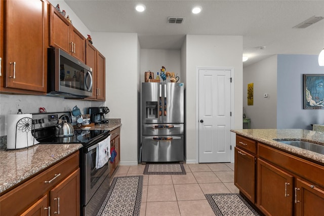 10626 Laguna Plains Dr, Riverview, FL 33578 - kitchen featuring stainless steel appliances, stone counters, light tile patterned flooring, recessed lighting, and brown cabinetry