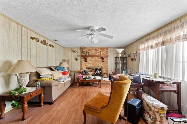 living room featuring wood walls, a textured ceiling, visible vents, ceiling fan, and light wood-style flooring