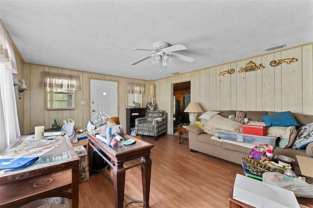 living room featuring wood walls, a textured ceiling, visible vents, and wood finished floors