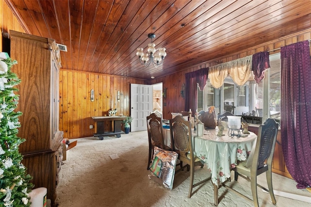 carpeted dining area featuring wooden walls, an inviting chandelier, visible vents, and wooden ceiling