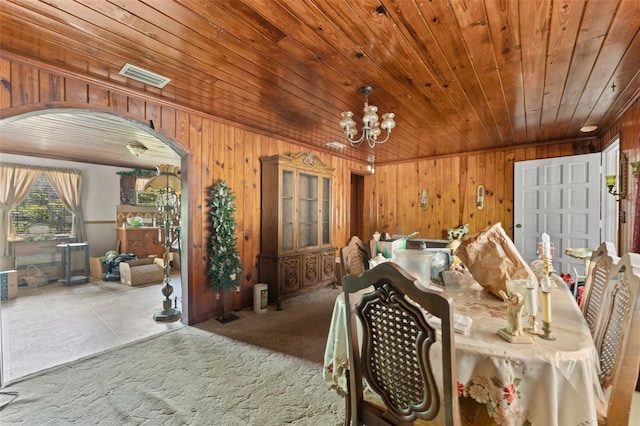 carpeted dining area featuring an inviting chandelier, wood ceiling, visible vents, arched walkways, and wooden walls