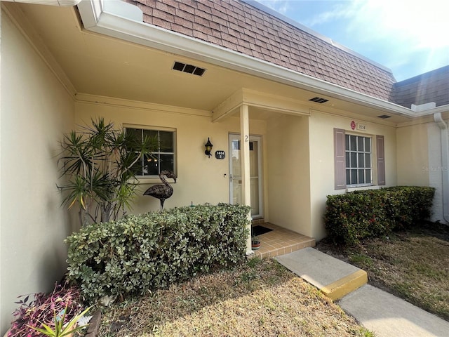 property entrance with a shingled roof, mansard roof, and stucco siding