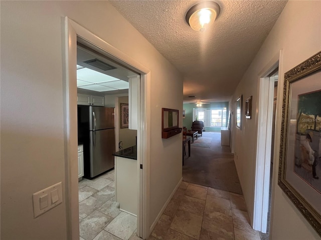 corridor with stone tile floors, a textured ceiling, and baseboards