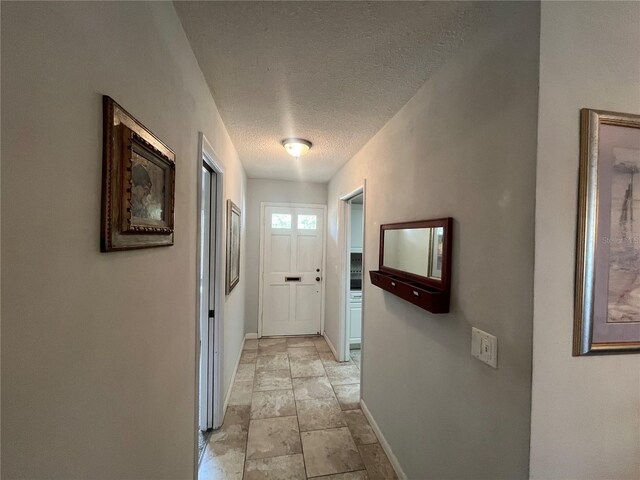 corridor with baseboards, a textured ceiling, and light stone finish flooring