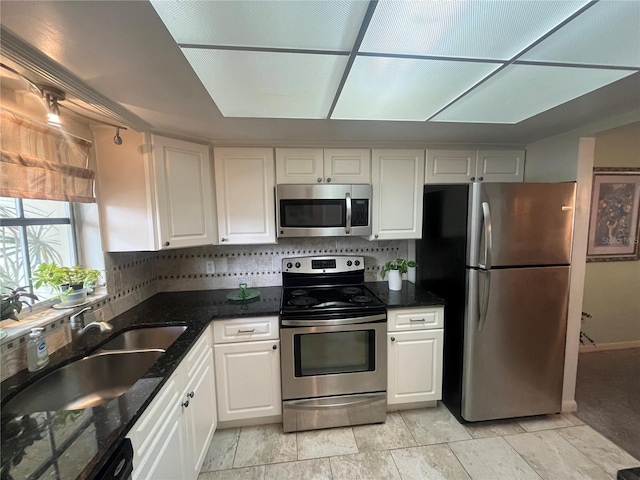 kitchen with appliances with stainless steel finishes, white cabinetry, a sink, backsplash, and dark stone counters