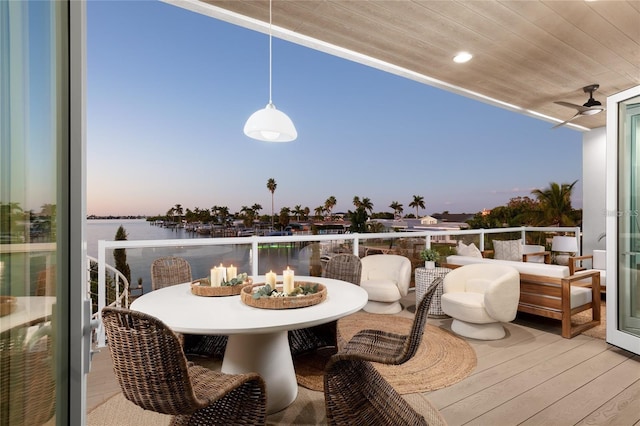 balcony at dusk with a water view, outdoor dining area, and a ceiling fan