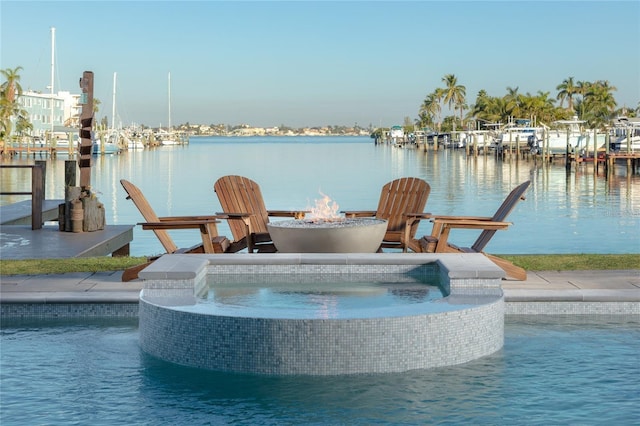 view of pool featuring a pool with connected hot tub, a water view, a fire pit, and a dock