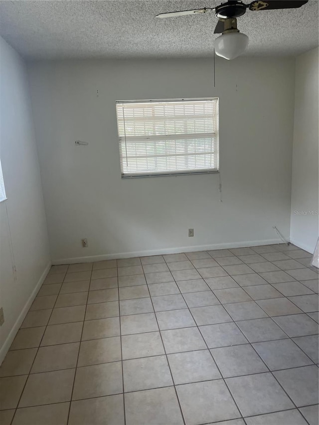 empty room with a textured ceiling, baseboards, light tile patterned floors, and ceiling fan