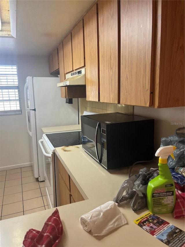 kitchen featuring under cabinet range hood, black microwave, light countertops, light tile patterned floors, and electric range
