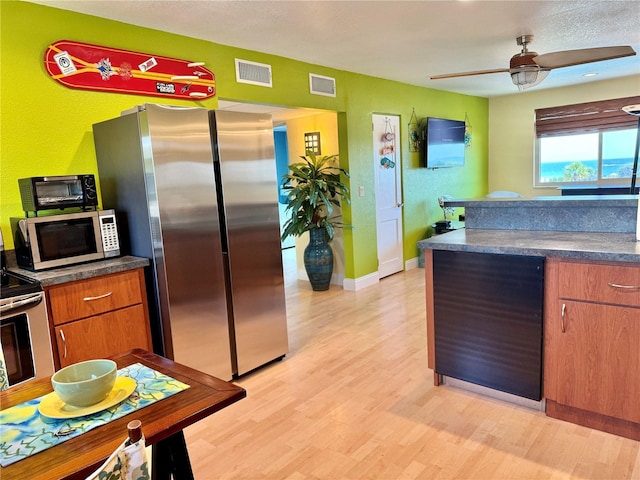 kitchen with light wood-type flooring, stainless steel appliances, dark countertops, and visible vents